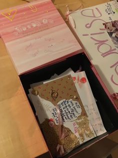 an open pink box filled with lots of cards and paper on top of a wooden table