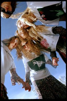 three young women are standing together in front of the camera, with their hair blowing in the wind