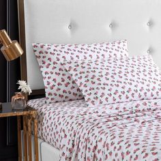 a white bed with pink and red flowers on it, next to a night stand