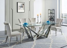 a glass dining table with white chairs and candles on the table in front of a large window