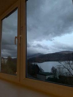 a window with a view of a lake and mountains in the distance, looking out at dark clouds