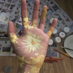 a person's hand with yellow paint on it and other art supplies in the background