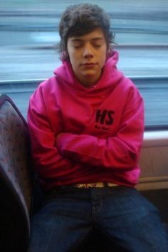 a young man in a pink hoodie sitting on a train