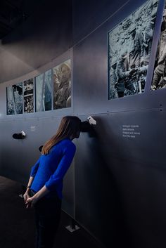 a woman standing next to a wall with pictures on it and looking at something in the distance