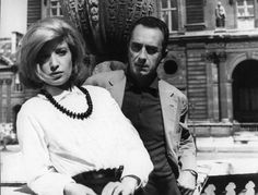 a man and woman sitting on a bench in front of a building with an ornate sculpture behind them