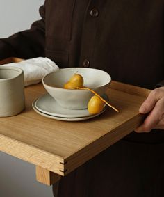 a person holding a plate with two pears in it and a cup on the table