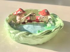 two little figurines are sitting in a bowl with water and mushrooms on it