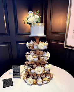 a three tiered cake with cupcakes and flowers on the top is sitting on a table