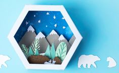 an origami box with mountains, trees and bears in it on a blue background