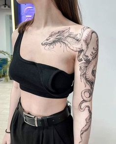 a woman with a dragon tattoo on her arm and shoulder, standing in front of a wall