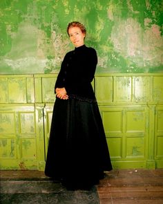 a woman in a long black dress standing next to a wall with green paint on it