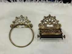 two antique brass toilet paper holders on a white sheet with feathers in the back ground