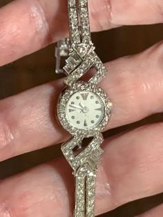 This stunning piece of fine jewelry is a vintage platinum and diamond Le Coultre lady's watch. There are 22 round single cut diamonds set around the case, each .01 ct. The case connector has 12 round single cut diamonds, 11 @ .02, 1 @ .04, and 3 straight baguettes, 1 @ .02, 1 @ .03, and 1 @ .05 cts. This identical pattern of diamonds repeats on the other side of the case. The band consists of 11 links that hold 4 @ .02 ct. single cut diamonds per link, 1 link of 3 straight baguettes diamonds @ 0 Classic Diamond White Watch With Brilliant Cut, Classic Diamond White Round Diamond Watch, Classic Round Diamond Watch For Formal Occasions, Classic Diamond Watch For Formal Occasions, Classic Diamond Jewelry With Brilliant Cut, Diamond Watch With Brilliant Cut, Classic Diamond White Watch For Anniversary, Timeless Diamond Watch With Diamond Hour Markers, Timeless Round Diamond Watch With Diamond Hour Markers