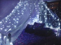 a bed covered in white lights next to a window with curtains on top of it