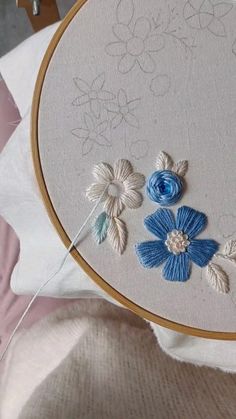 a close up of a embroidery on a white cloth with blue flowers and leaves in the center