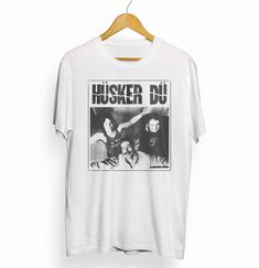 a white t - shirt with the words husker du on it hanging from a wooden hanger