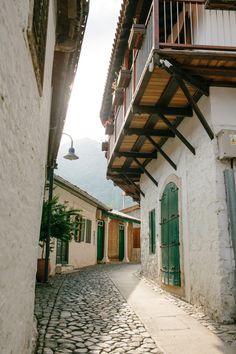 a cobblestone street in an old town with white buildings and green shutters