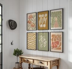 four framed art pieces hang on the wall next to a wooden table with a potted plant