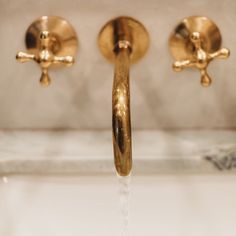 two golden faucets are running water from the sink