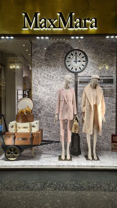 two mannequins in front of a store window display with luggage and clocks