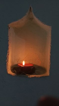 a lit candle in a white wall with a small hole between it and someone's hand