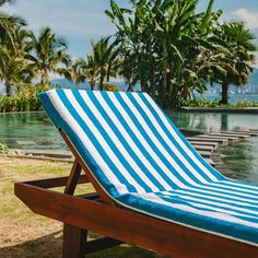 a blue and white striped beach chair sitting on the side of a swimming pool with palm trees in the background