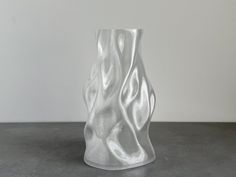 a white glass vase sitting on top of a table next to a wall and floor