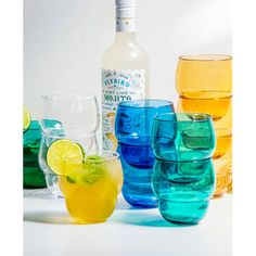 there are many different colored glasses next to each other on the table with a bottle in the background