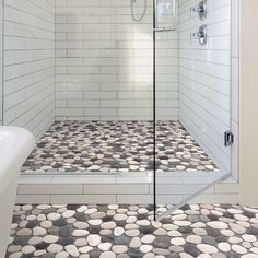 a walk in shower sitting next to a white bath tub under a window with rocks on the floor