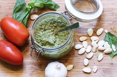 tomatoes, basil, garlic and almonds on a cutting board with pesto in a jar