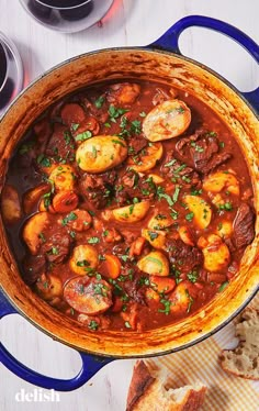 a large pot filled with stew and bread on top of a white table next to wine glasses