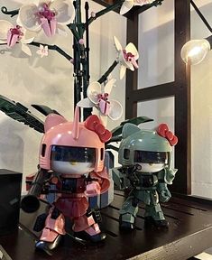 two toy figurines sitting on top of a table next to a flower tree