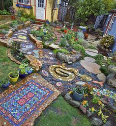 an outdoor garden with lots of plants and rocks on the ground in front of a house