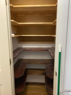 an empty closet with wooden shelves and benches in the corner, next to a white door