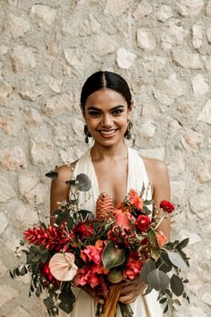 a woman holding a bouquet of flowers in front of a stone wall