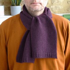 a man wearing an orange sweater and purple scarf with a potted plant in the background