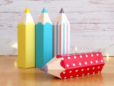 three colored pencils are next to each other on a wooden table with lights in the background