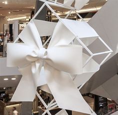 a large white bow hanging from the side of a ceiling in a store with people walking by