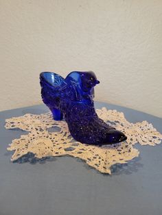 a blue glass shoe sitting on top of a white lace doily covered tablecloth