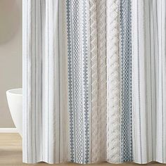 a white shower curtain with blue and grey stripes on it in a bathroom next to a bathtub