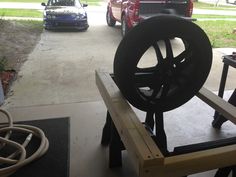 a car is parked in the garage next to a large wheel on a stand with wheels attached