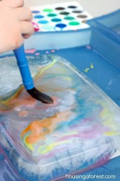 a child using a brush to paint on a piece of paper with watercolors