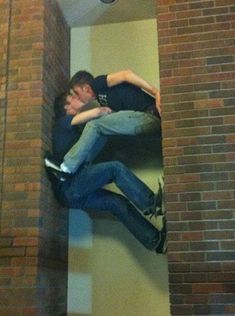 two men are hanging upside down on a brick wall, one is holding the other's head