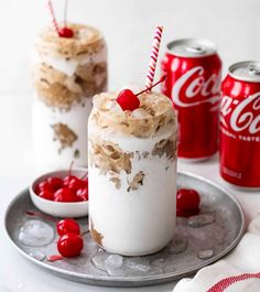 two desserts on a plate with coca - cola cans in the background and cherries