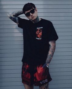 a man with tattooed arms and legs standing in front of a garage door wearing sunglasses