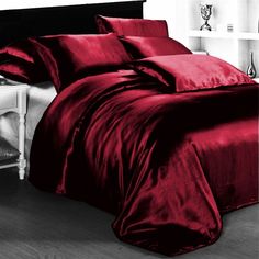 a bed covered in a red comforter next to a night stand with a lamp on it