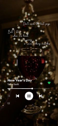 someone holding up a glass of wine in front of a christmas tree with the words new year's day written on it