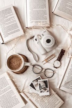 an assortment of books, camera, and other items on a white sheet with string lights