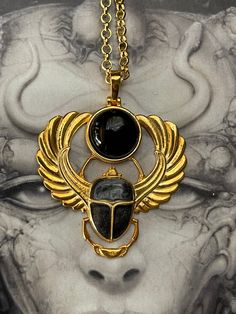 a woman's face with gold wings and a black stone pendant on a chain