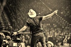 a man wearing a cowboy hat and suspenders standing in front of a crowd with his arms outstretched